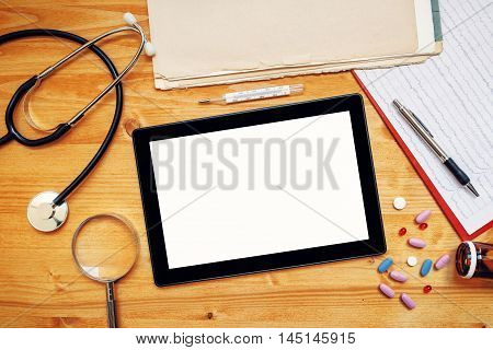 Tablet computer with blank screen on doctor's office desk as copy space top view of general medical practitioner accessories in workspace.