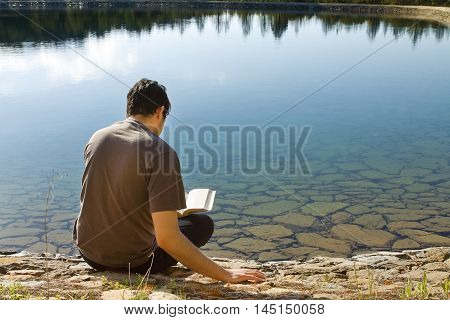 Man reading Book by Beautiful lake to Relax