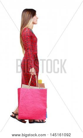 side view of going woman with shopping bags . beautiful girl in motion. girl in red plaid dress goes sideways holding up paper bags.