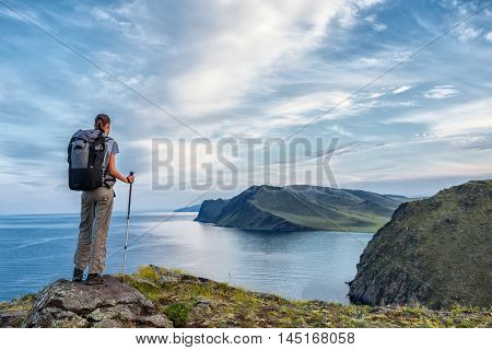 Young woman with backpack look at lake from high point of view.
