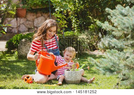 Pregnant woman with little daughter in the summer orchard cearing flower.