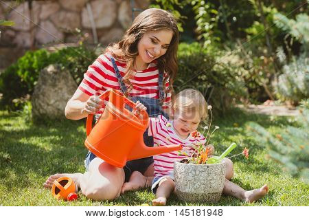 Pregnant woman with little daughter in the summer orchard cearing flower.