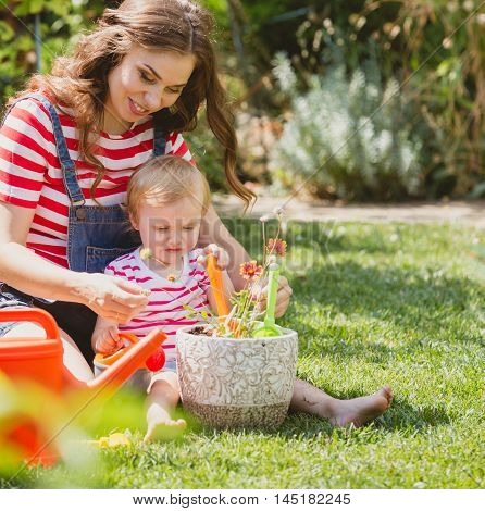 Pregnant woman with little daughter in the summer orchard cearing flower.
