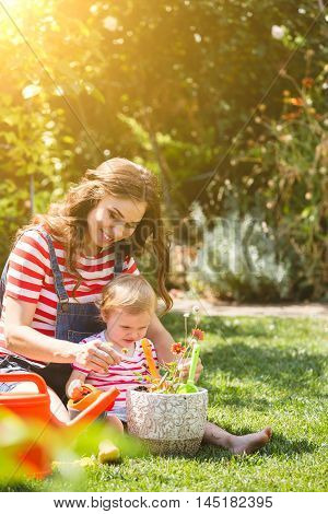Pregnant woman with little daughter in the summer orchard cearing flower.