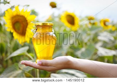 Woman holding bottle of honey on sunflower field background