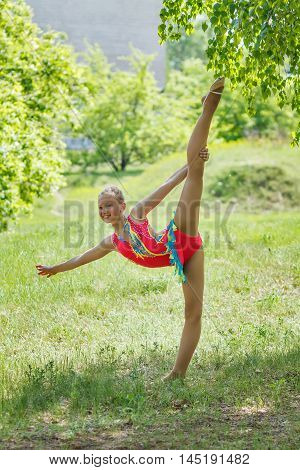 Gymnast-girl is exercising at the green meadow