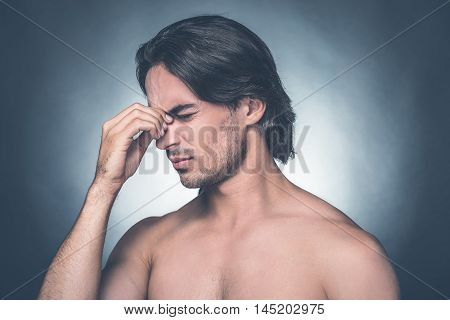 Feeling stressed. Portrait of frustrated young shirtless man keeping eyes closed and massaging his nose while standing against grey background