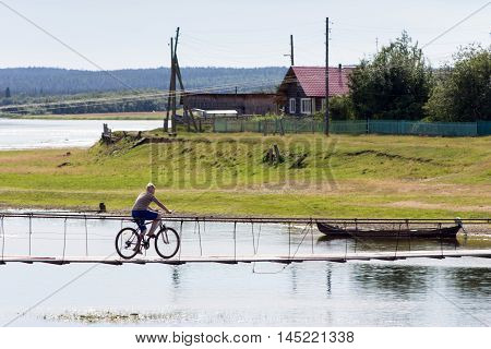 Zagrivochnaya Russia - 24.07.2016 Rural landscape at summer with boy on bicycle rides on wooden suspension bridge