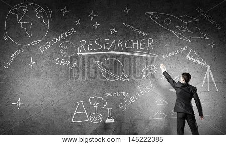 Rear view of man drawing education concept on blackboard with chalk