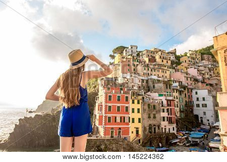 Young female traveler in blue dress enjoying great view on the old coastal town in Riomaggiore on the northern Italy