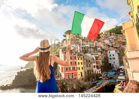 Young female traveler with italian flag enjoying great view on the old coastal town in Riomaggiore on the northern Italy. Promoting tourism in Italy