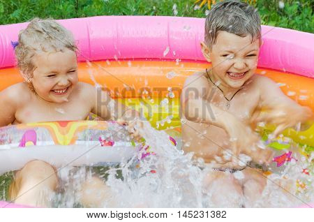 Two children happily laughing and floating in an inflatable swimming pool in summer outdoors