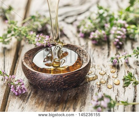 Herbal honey pouring into the wooden bowl. Bowl is on old wooden table surrounded with levender flowers.