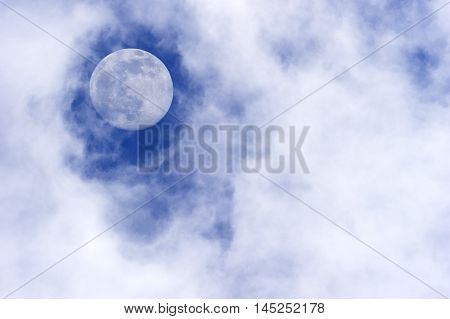 Moon clouds is a daytime scenic of wispy white cumulus clouds set against a deep blue sky as a full moon rises in the sky.