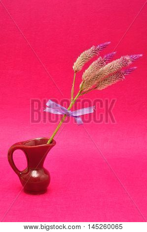 Purple flowers tied with a purple bow displayed in a maroon flower pot isolated on a pink background