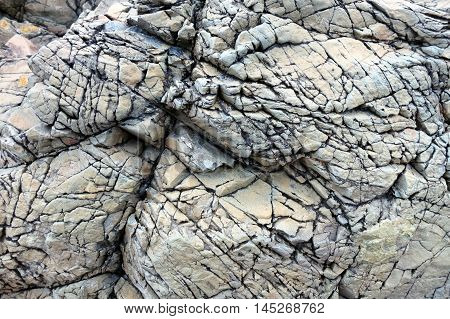 Rock textured with deep cracks and shades of grey along the coast of Llanddwyn Island, Anglesey, Wales.