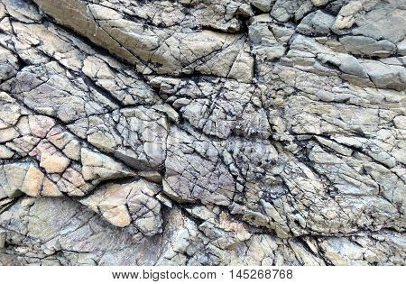 Rock textured with deep cracks and shades of grey along the coast of Llanddwyn Island, Anglesey, Wales.