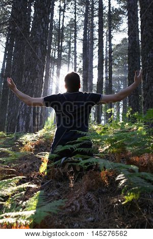 Man Kneeling in the forest with arms lifted up
