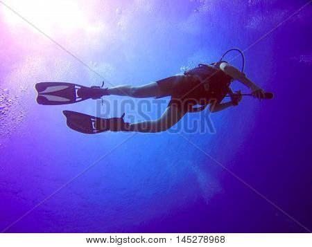 A backlit scuba diver silhouette. View of the scuba diver gear fins and bubbles underwater in the deep blue sea of Limassol Cyprus against the sunlight.