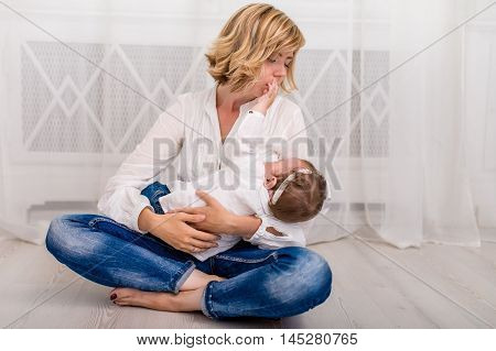 Young mother breastfeeding her child baby girl lying on her breast and feeding on a whine background