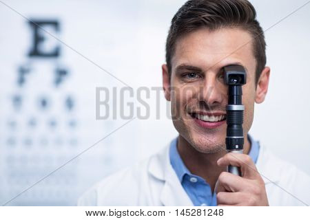 Close-up of smiling optometrist looking through ophthalmoscope in ophthalmology clinic