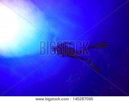 A backlit scuba diver silhouette. View of the scuba diver gear fins and bubbles underwater in the deep blue sea of Limassol Cyprus against the sunlight.