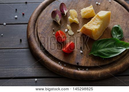 Cheese delikatessen closeup on rustic wood. Wooden desk with parmesan, camembert and brie cuts decorated with garlic, tomato and basil