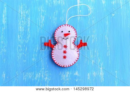 Fun felt Christmas snowman ornament isolated on a blue wooden background. How to make a Christmas snowman ornament. Step. Christmas tree decor idea for chilfren. Easy felt sewing crafts. Top view