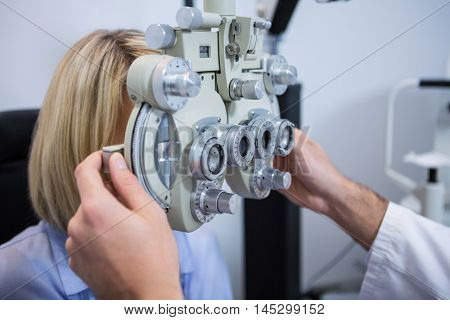 Female patient under going eye test through phoropter in ophthalmology clinic