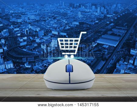 Wireless computer mouse with on line shopping icon on wooden table over city tower street and expressway