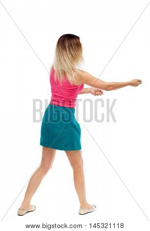 back view of standing girl pulling a rope from the top or cling to something. Isolated over white background. Blonde in a red sweater and green skirt pulling rope.