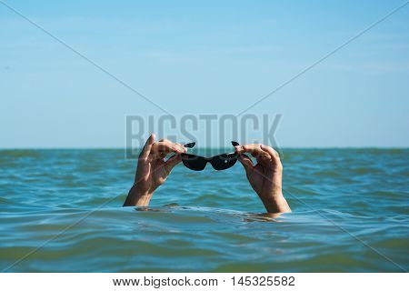 The man in the sea is holding sunglasses above the water