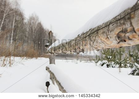old rough rustic fence, made of logs, covered with snow
