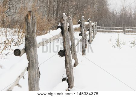 old rough rustic fence, made of logs, covered with snow