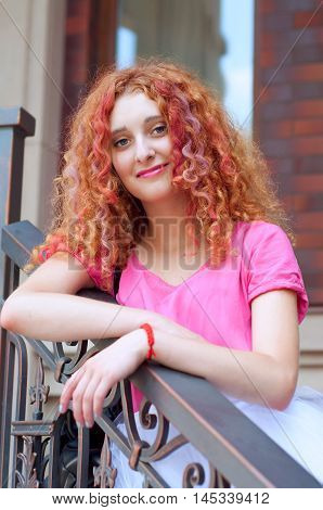 Happy smiling beautiful young woman with curly red hair with colorful hair pieces wearing bouffant skirt and magenta blouse standing on staircase