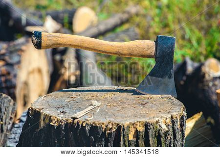 Old worn scratched sharp ax standing on a wooden cracked tree stump on a background of chopped wood.