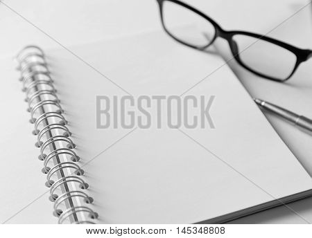 White blank notebook with silver pen and glasses. Some money and wallet are located close to it.