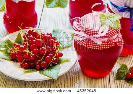 Preserved homemade red currant jam in glass jars on white wooden table. Fresh berries and green leaves vintage plate.