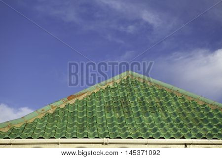 Green roof tiles set against blue sky with wispy clouds providing copy space.