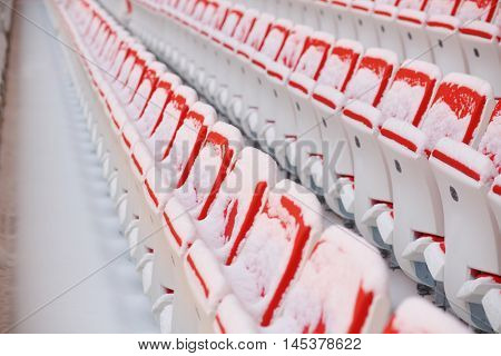 Rows of red empty seats of grandstands covered by snow on stadium