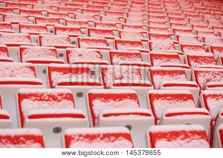 Rows of bright empty seats of grandstands covered by snow on stadium