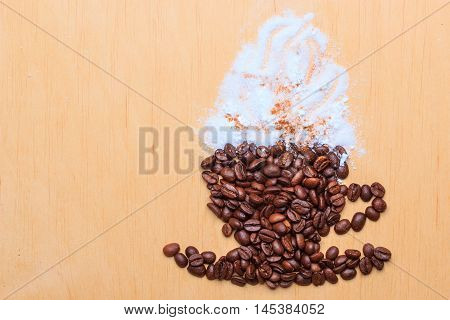 Cappuccino time. Roasted coffee beans placed in shape of cup and saucer with cinnamon white froth on wooden surface background