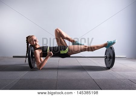 fitness, sport, exercising hard working concept - smiling young woman on the barbel showing thumbs up in gym