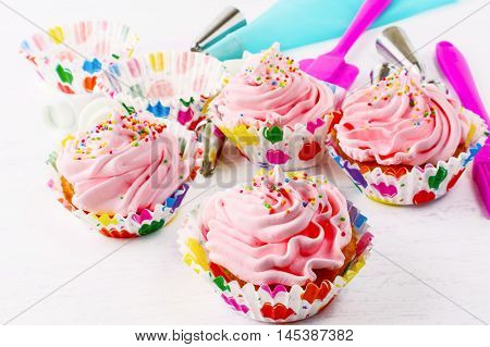Homemade pink birthday cupcakes and cookware background. Birthday cupcake with pink whipped cream. Homemade cupcakes decorated for party.
