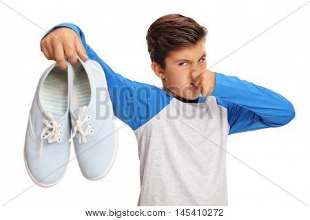 Disgusted boy holding a pair of smelly shoes isolated on white background