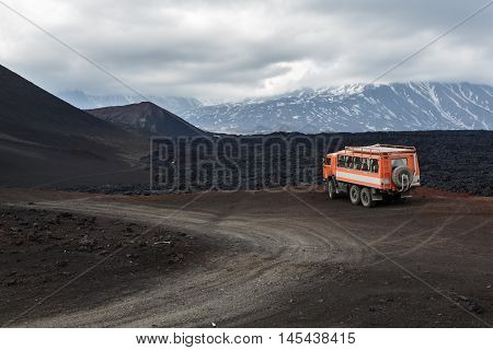 KAMCHATKA PENINSULA RUSSIA - JUNE 24 2016: Russian expedition truck KamAZ (6-wheel drive) on mountain road on background of lava fields and volcanoes. Eurasia Far East Russia Kamchatka Region Klyuchevskaya Group of Volcanoes.