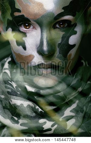 Beautiful young fashion woman with military style clothing and face paint make-up, khaki colors, halloween celebration close up, green pattern all over body