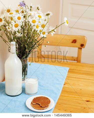 Simply stylish wooden kitchen with bottle of milk and glass on table, summer flowers camomile, healthy foog moring concept close up