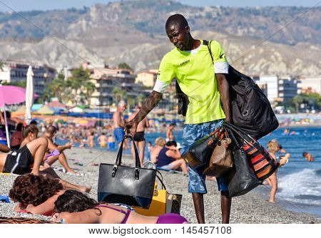 MARINA DI GIOIOSA IONICA, ITALY - AUGUST 16: An seller of handbags try to sell a bag to tourists on the beach. Taken on August16. 2015 in Marina di Gioiosa Ionica, south Italy.