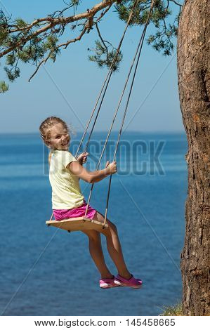 little girl swinging on seesaw above a sea